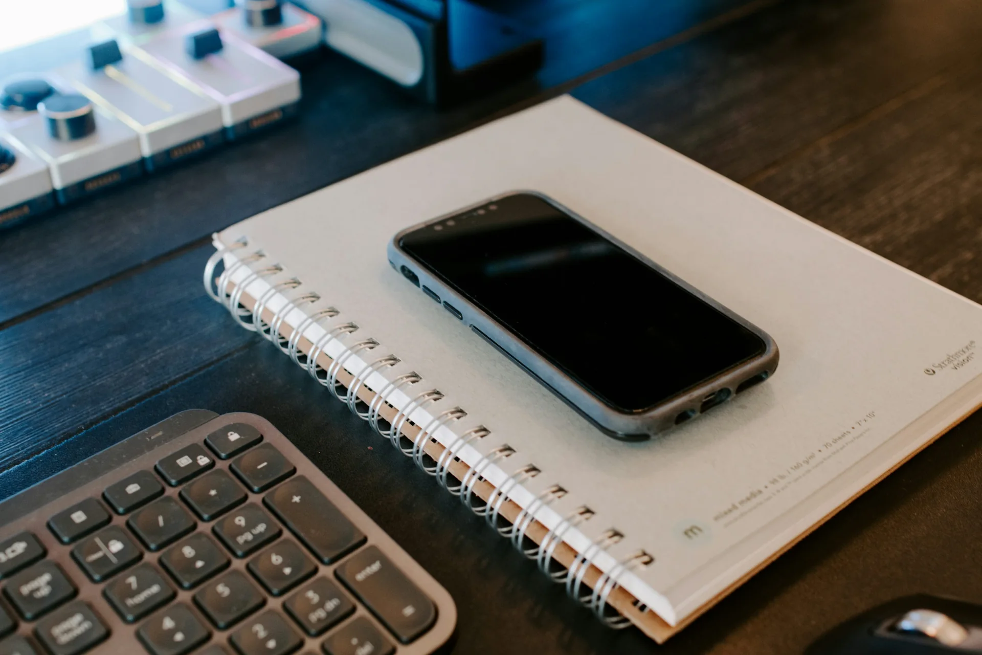 Phone resting on a spiral notebook beside a computer keyboard