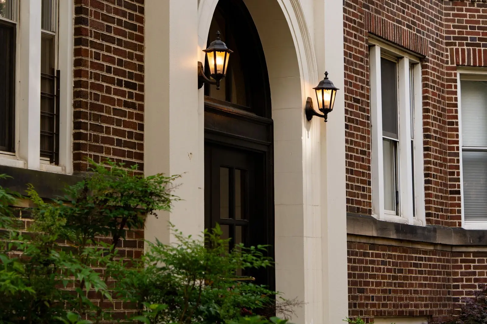 The arched entrance of a red-brick apartment building, its two lanterns still lit in the early morning.