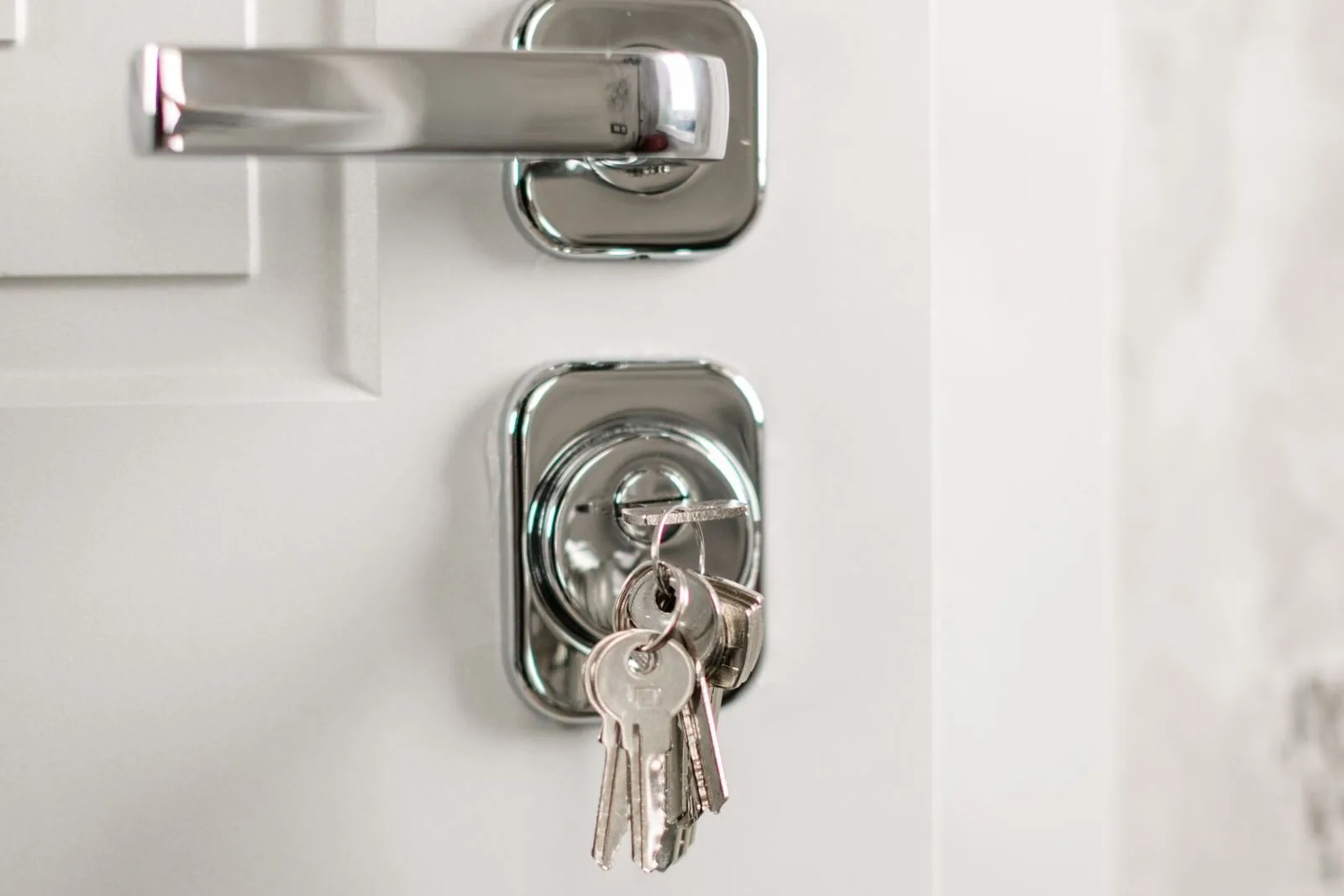 A white apartment door with a chrome lever handle and a keyed deadbolt with a set of keys hanging from it.