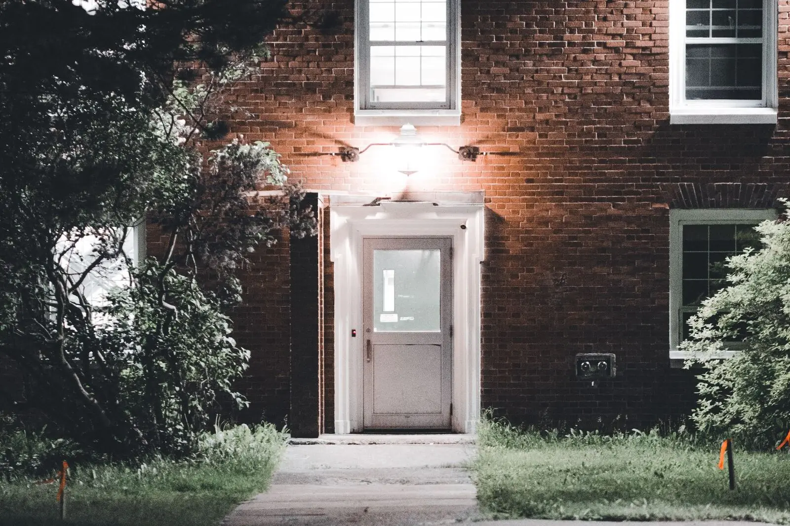 A white front door in a red-brick building, lit by a single lamp above it at night.
