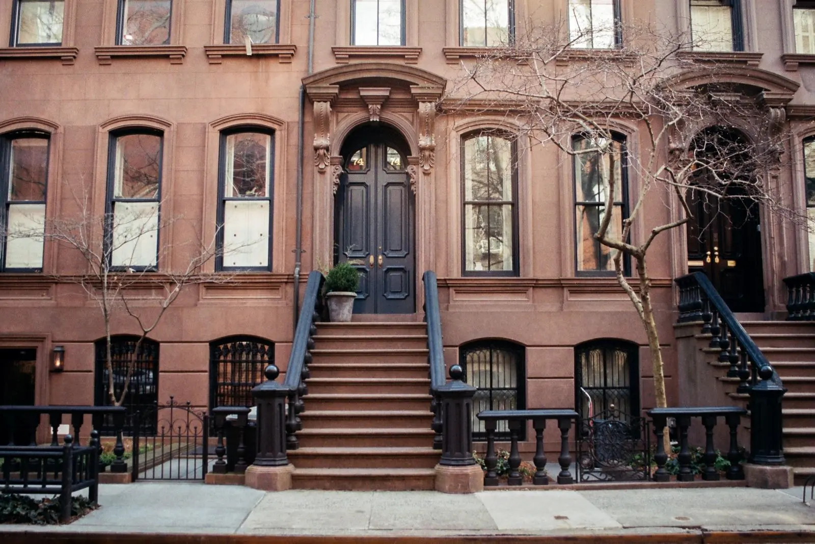 A row of brownstones with high stoops and black iron railings, double entry doors at the top of the steps.
