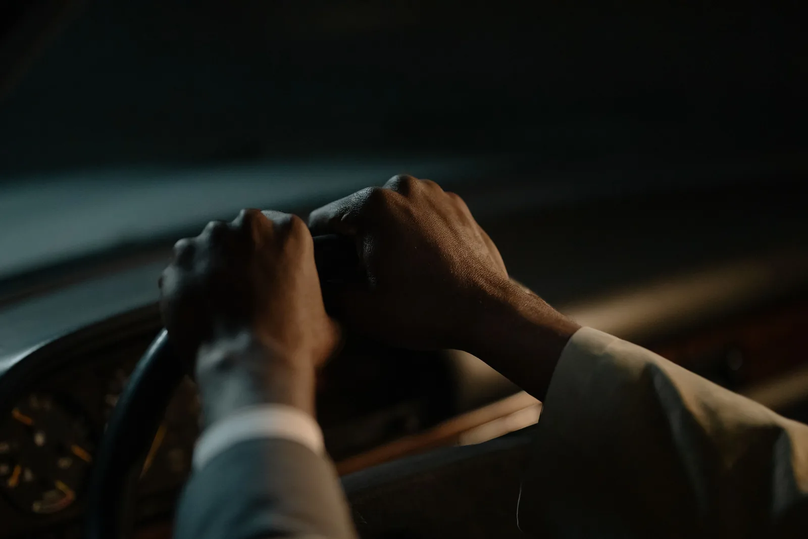 Close-up of a driver's hands gripping the steering wheel of a car at night, in dim, warm light.