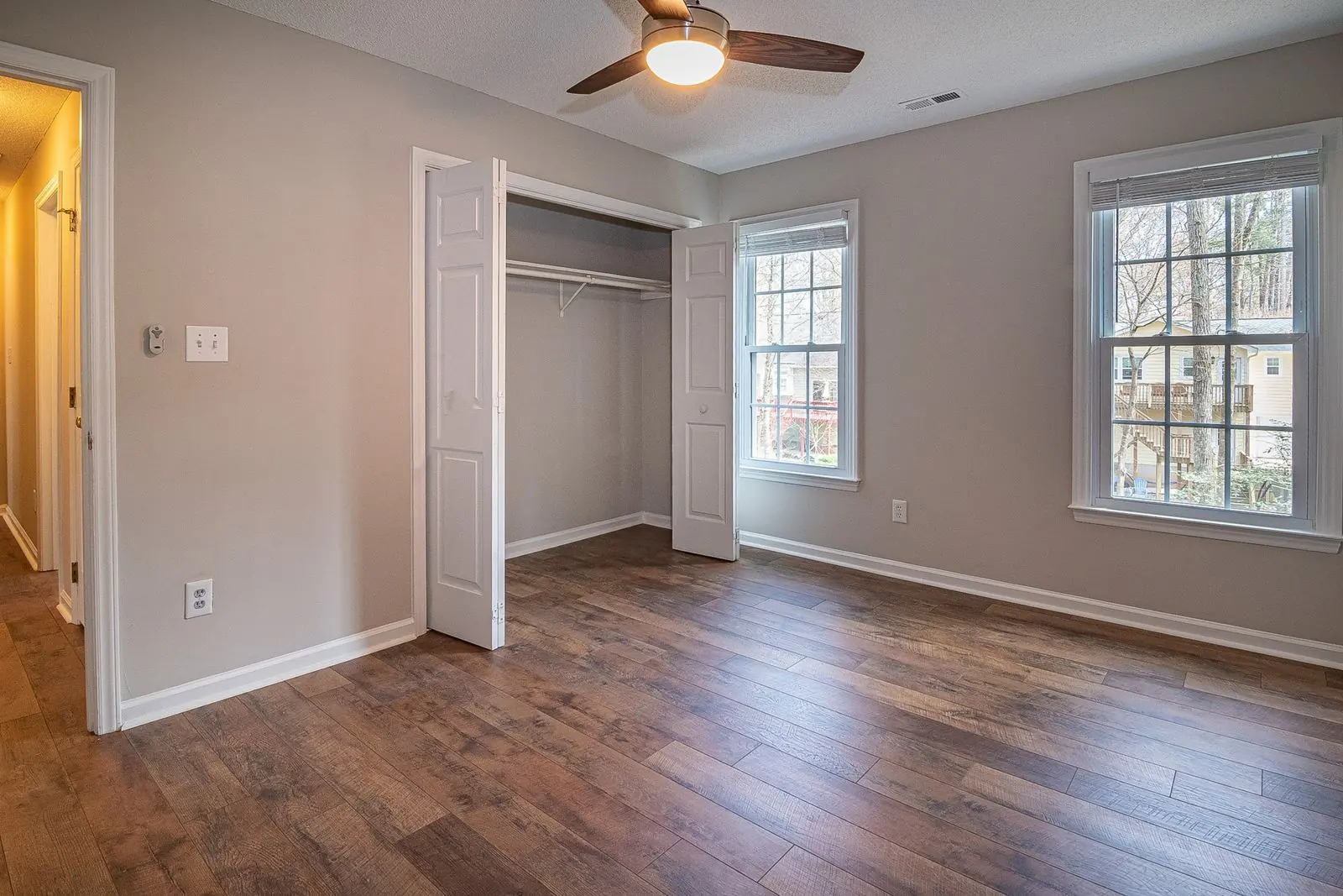 An empty bedroom with wood floors, an open closet and two windows, ready for a new tenant.