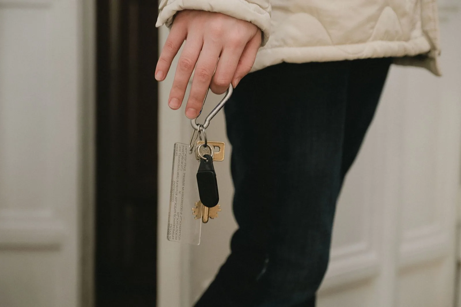 A person in a light jacket holding a set of keys on a clip beside an open apartment door, face not shown.