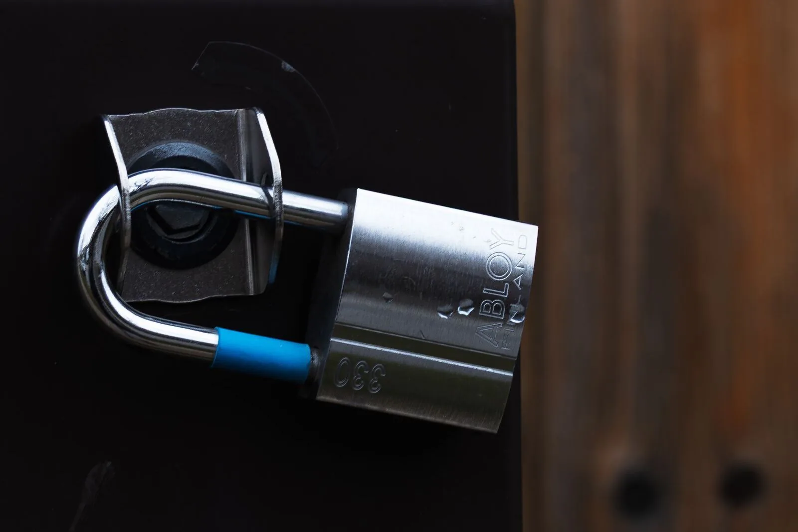 A high-security padlock with a steel body and a blue-sleeved shackle, fixed to a black cabinet door.