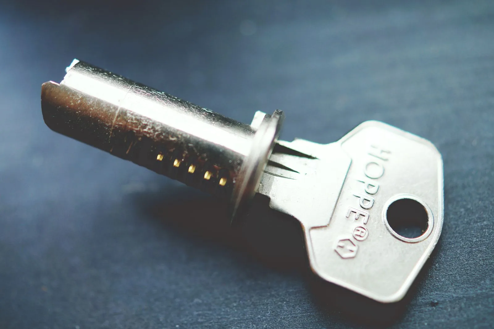 A lock cylinder plug with its key beside it, photographed on a dark slate surface.