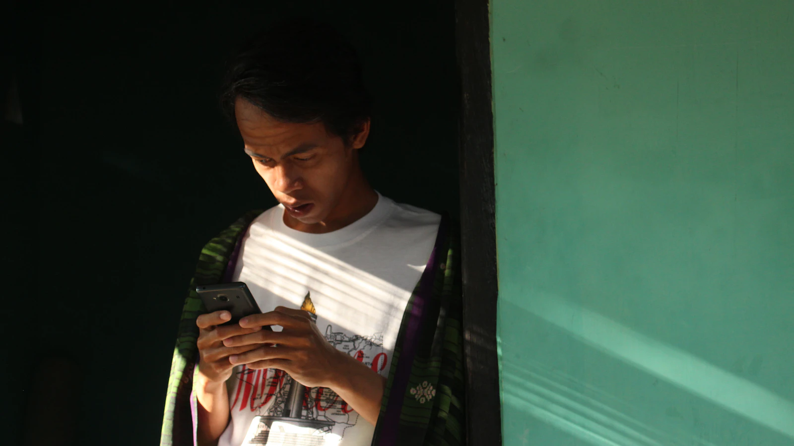 A person looks at a smartphone while standing in a doorway.