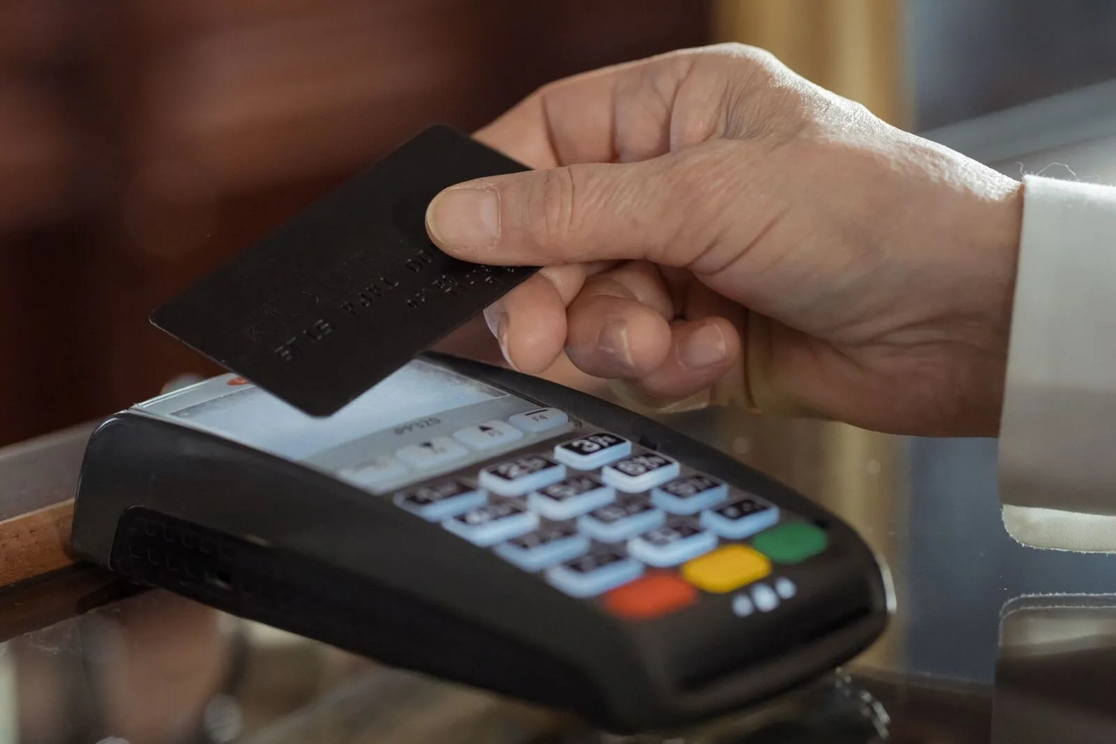 A hand holding a black payment card just above a card terminal, about to tap to pay.
