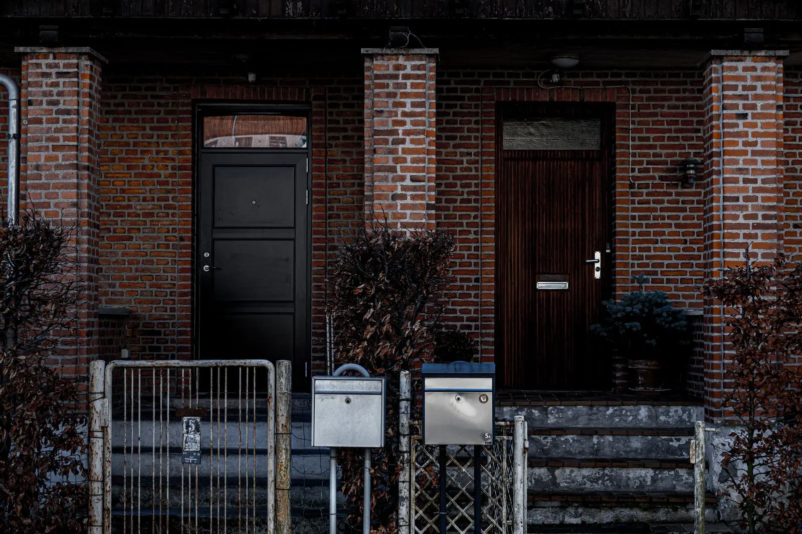 Two neighboring brick row houses in New York City, each with its own front door, metal gate and mailbox at the foot of the steps.
