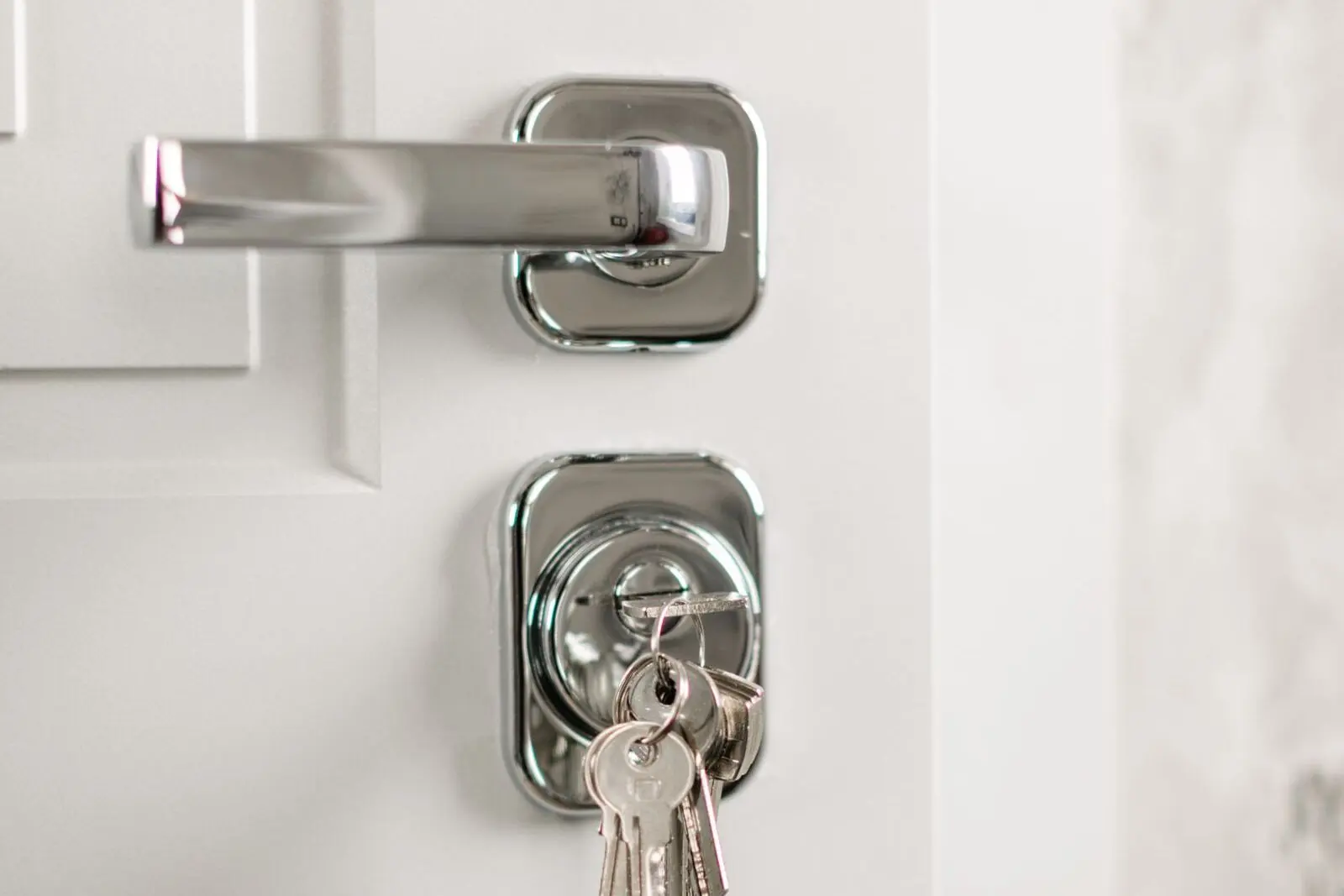 A white apartment door with a chrome lever handle and a separate keyed lock below it, keys hanging from the cylinder.